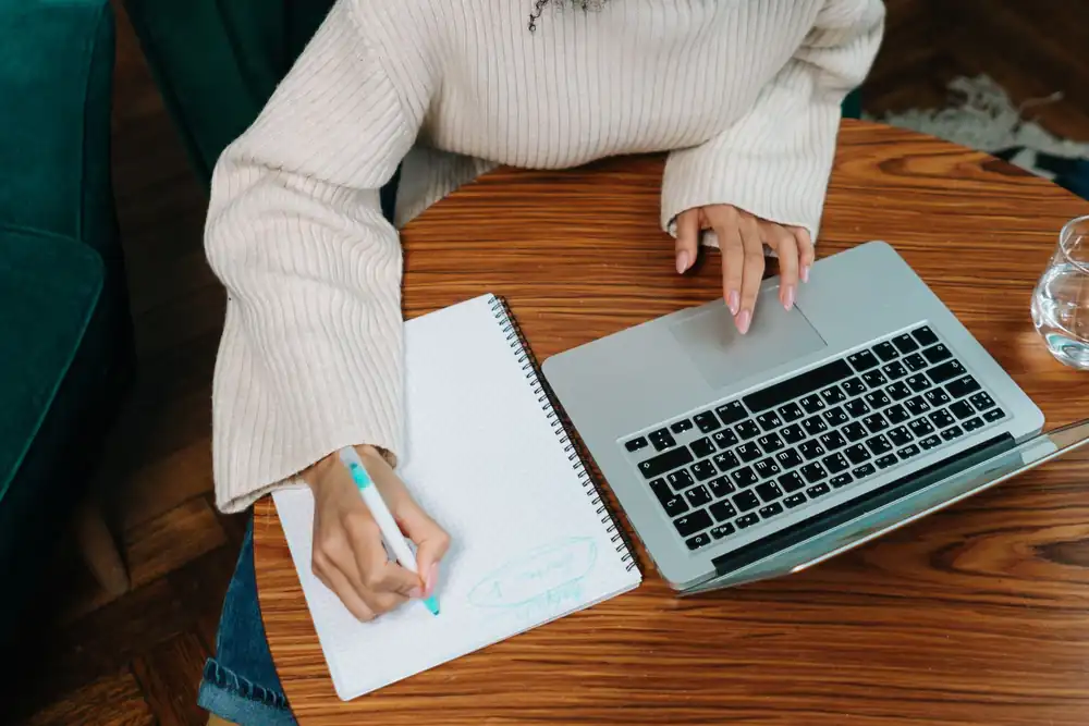 Researcher writing notes in a notebook while working with a laptop